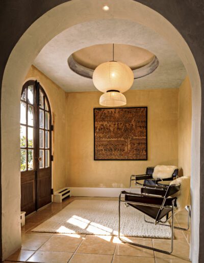 An elegant arched nook featuring a modern chair with a sheepskin throw, a round pendant light, and an intricate wall art piece.