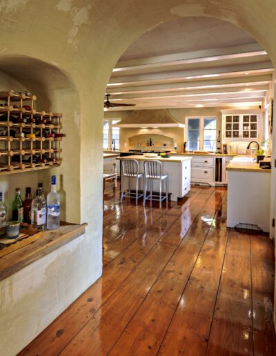 Spacious kitchen interior featuring an archway, a wooden wine rack, and a central island with bar stools.